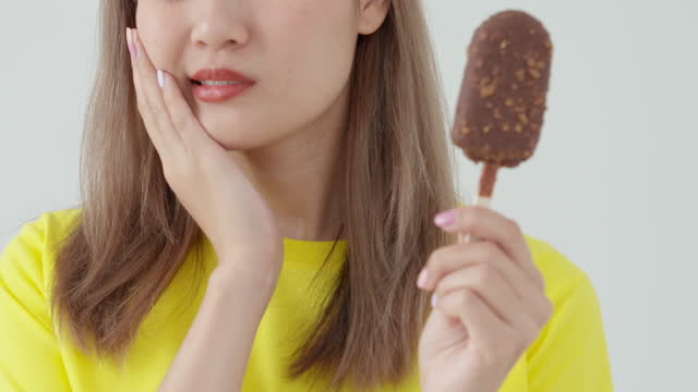 a woman in yellow shirt with sensitive tooth cupping her jaw while holding an ice-cream